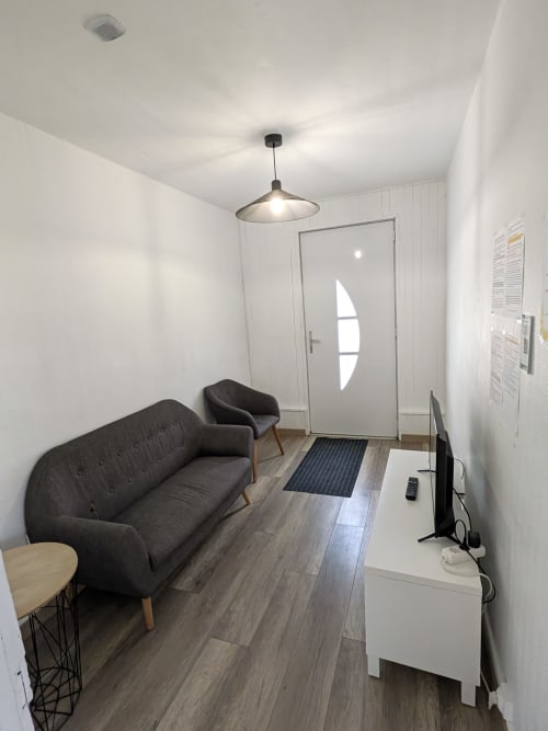 Salon moderne à la Résidence des dunes à Landéda : canapé gris, fauteuil sombre, TV et porte d'entrée blanche