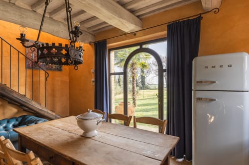Sala da pranzo in rustico italiano con pareti arancioni, travi in legno, finestra ad arco con vista sulla campagna e frigorifero SMEG vintage