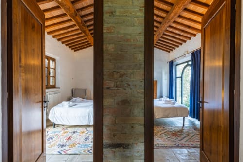 Due suite con travi in legno, colonne rustiche e tende blu presso l'hotel Quarantallina a Buonconvento, Toscana