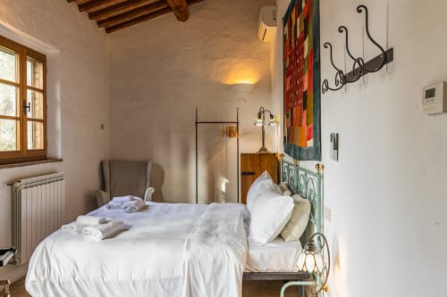 Camera da letto rustica dell'hotel Buonconvento con letto in ferro, biancheria bianca, travi in legno e arredamento tradizionale