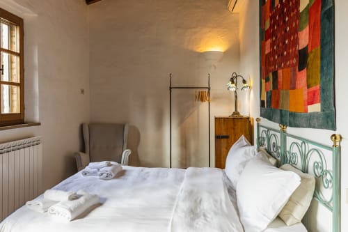 Camera luminosa all'hotel Quarantallina di Buonconvento con biancheria bianca, letto in ferro verde e arte tessile colorata