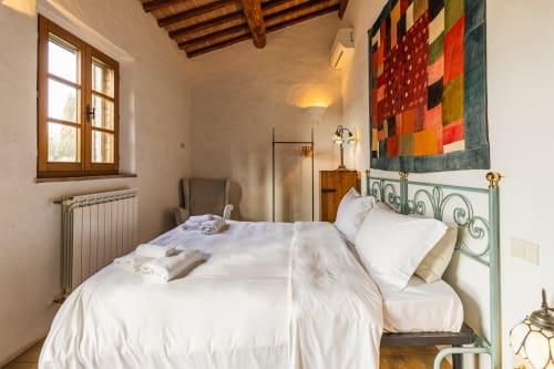 Camera da letto dell'agriturismo toscano con letto in ferro battuto, coperta patchwork colorata, travi in legno e fascino rustico a Buonconvento