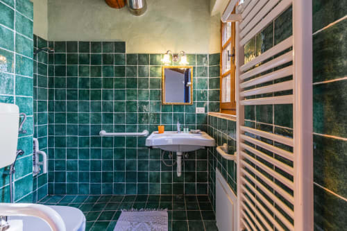 Moderno bagno con piastrelle verdi nell'aparthotel Buonconvento: lavabo su piedistallo, specchio e scaldasalviette