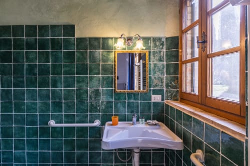 Bagno con pareti piastrellate verdi, specchio, lavabo e finestra nell'appartamento dell'hotel Buonconvento