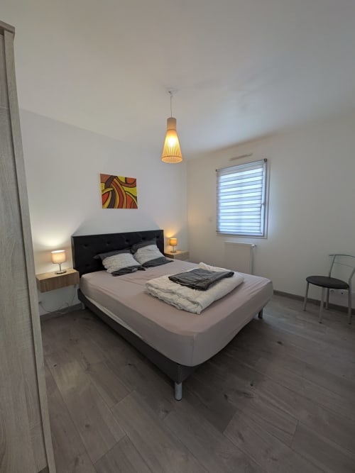 Chambre moderne à la Résidence des dunes à Landéda avec lit noir, luminaires suspendus chaleureux et vue sur le jardin