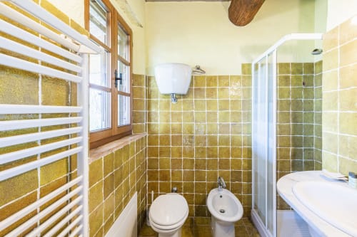 Bagno con piastrelle dorate alle pareti, wc, bidet, lavabo, radiatore bianco e doccia nell'appartamento dell'hotel Buonconvento