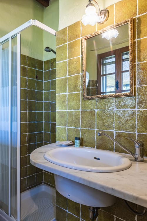 Bagno moderno con piastrelle verde oliva, lavabo a colonna, specchio e cabina doccia in vetro all'hotel Quarantallina