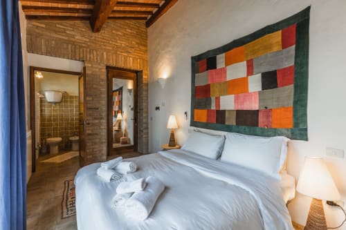 Camera da letto moderna a Buonconvento con arazzi colorati, letto matrimoniale e bagno con mattoni a vista