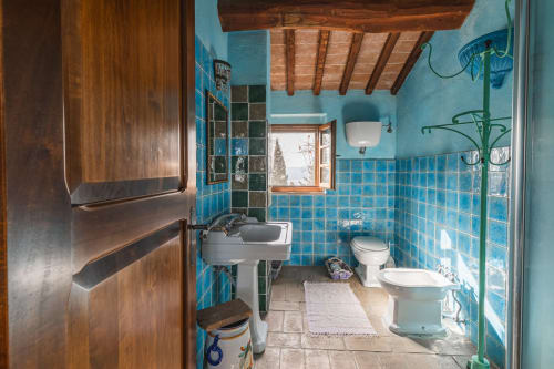 Bagno rustico dell'hotel Buonconvento con piastrelle turchesi, travi in legno e pavimento in pietra a vista