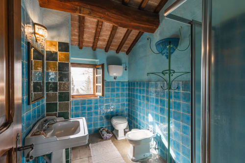Bagno rivestito di piastrelle blu con lavandino, toilette, doccia e soffitto con travi in legno all'hotel Quarantallina di Buonconvento, Italia