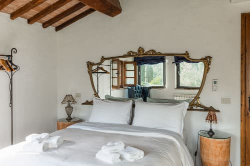 Camera da letto rustica con specchio ornato, biancheria bianca e travi in legno all'hotel Quarantallina di Buonconvento