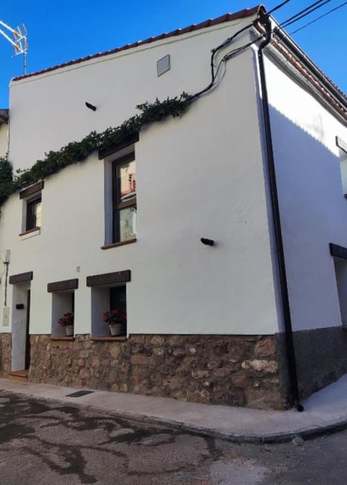 Casa Rural El Abuelo en Bronchales con paredes blancas, cimientos de piedra e hiedra trepadora