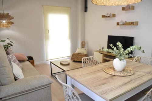 Luminosa sala de estar abierta en apartamento Casa El Abuelo con mesa de comedor, sillas blancas y jarrón blanco con plantas