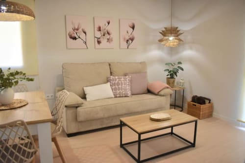 Luminoso salón en apartamento Casa El Abuelo con sofá beis, mesa de centro de madera, arte floral en pared y lámpara de tejido