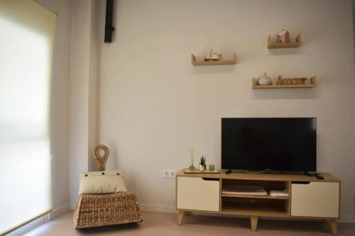 Sala de estar de apartamento de 1 dormitorio moderno con TV, estanterías de madera, detalles tejidos y decoración minimalista escandinava en Casa El