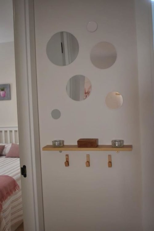 Pared de dormitorio con espejos circulares, repisa de madera con ganchos y objetos decorativos en Casa Rural El Abuelo