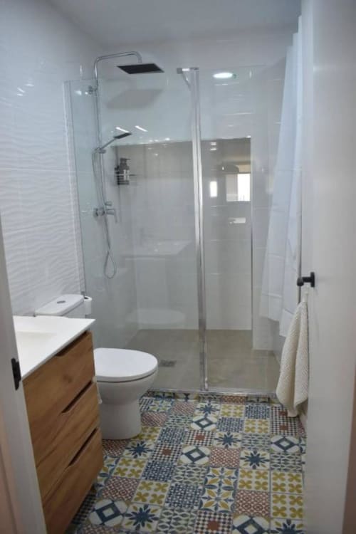 Baño moderno con ducha independiente, tocador de madera, inodoro y piso de azulejos con patrón en apartamento Casa El Abuelo