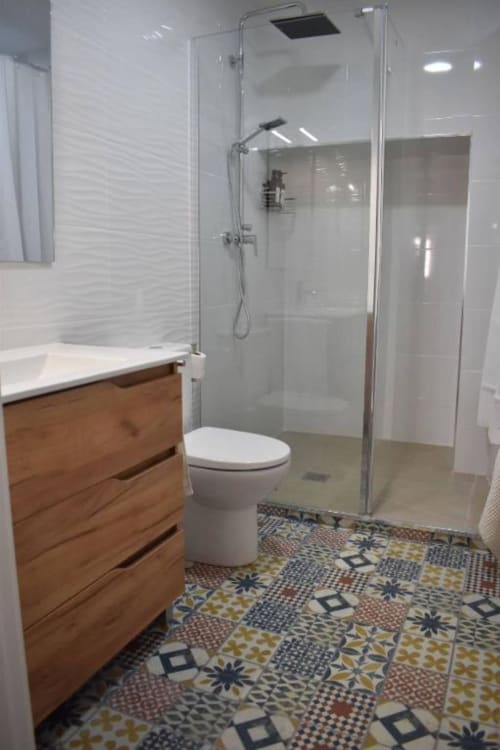 Baño moderno con tocador de madera, inodoro blanco, cabina de ducha de cristal y piso con azulejos estampados en Casa Rural El Abuelo
