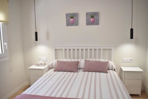 Dormitorio luminoso en apartamento rural Casa El Abuelo, Bronchales, con ropa de cama a rayas, almohadas rosas, cabecero blanco y