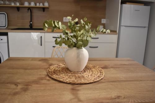 Jarrón de cerámica blanca con ramas de eucalipto sobre salvamanteles tejidos, mesa de comedor de madera en cocina moderna de Casa El Abuelo rural