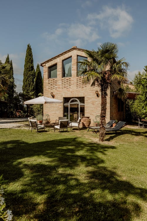 Rustico edificio in mattoni con palme e cipressi a Buonconvento, Italia, con zona living all'aperto
