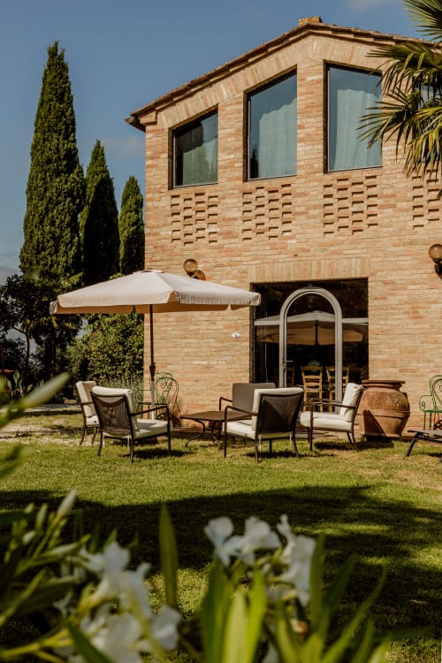 Appartamento in campagna toscana con terrazza in mattoni, zona salotto, ombrellone e cipressi a Buonconvento
