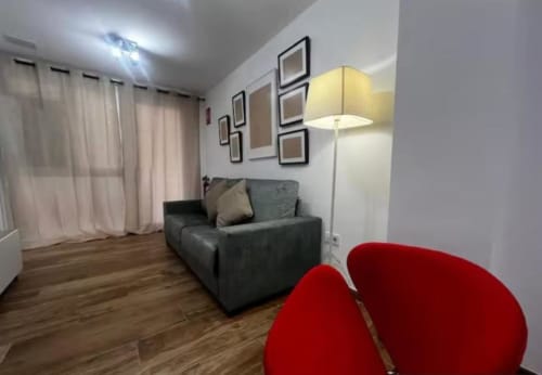 Moderna sala de estar en Las Arenas Valencia con sofá gris, sillas rojas y cuadros en la pared