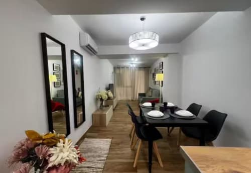 Zona de comedor del apartamento Las Arenas con mesa negra, espejos, suelos de madera e iluminación moderna en València