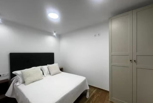 Moderno dormitorio en apartamento Las Arenas, Valencia con cama doble, cabecero negro, almohadas a cuadros y armario empotrado