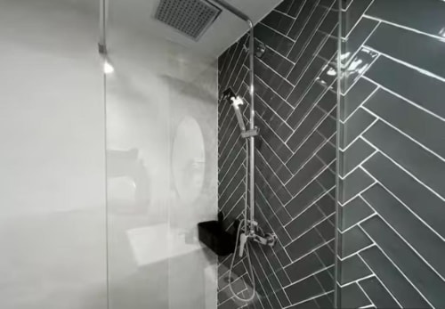 Baño moderno en apartamento Las Arenas con pared de azulejos en espiga oscura y mampara de ducha de cristal en València