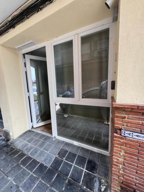 Entrada de apartamento moderno en Las Arenas Valencia con puertas de cristal blanco abiertas a patio de baldosas y pared de ladrillo