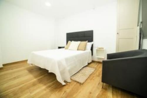 Dormitorio moderno en apartamento Las Arenas de València con cama de matrimonio, cabecero negro, suelos de madera y mobiliario contemporáneo
