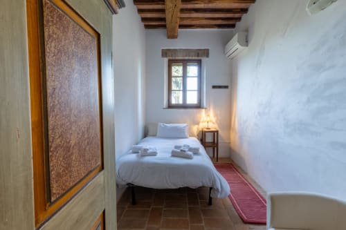Camera accogliente all'hotel Quarantallina a Buonconvento con pareti bianche, travi in legno, letto singolo e finestra con vista sul giardino
