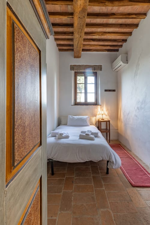 Camera rustica con travi in legno a vista, muri bianchi, letto singolo, finestra e pavimento in cotto all'hotel Quarantallina