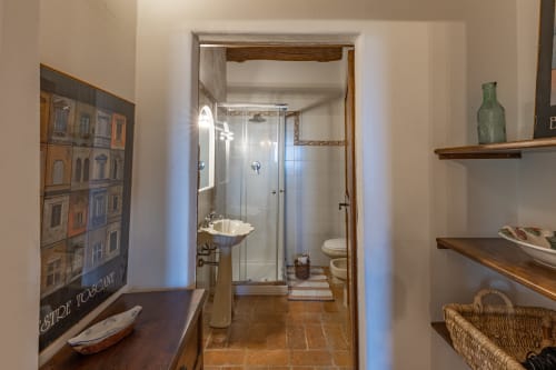 Bagno con doccia nell'appartamento di Buonconvento. Ripiani in legno, pareti bianche, pavimenti in cotto e arredamento italiano.
