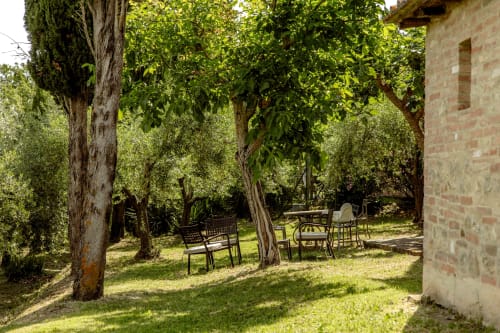 Area relax in giardino ombreggiato con alberi adulti e edificio in pietra dell'hotel Quarantallina a Buonconvento, Toscana
