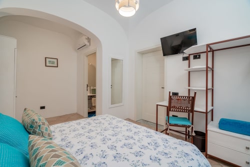Camera moderna a Short Let's Olbia con letto matrimoniale, accenti turchesi, scaffalature in legno, TV e bagno ensuite