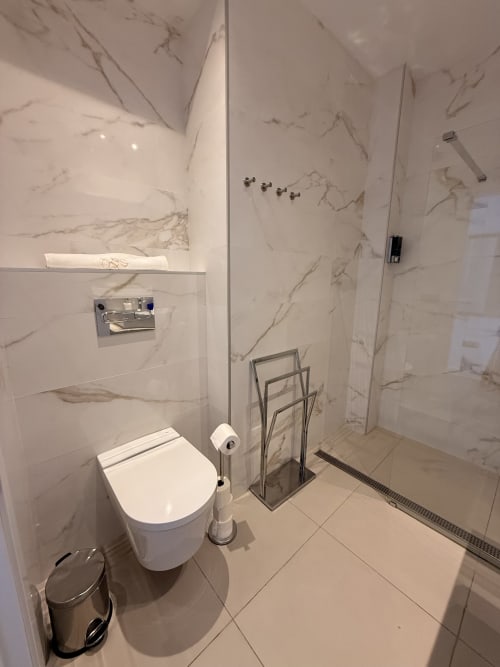 Baño moderno en suite de hotel Sevilla con paredes de mármol, inodoro blanco, ducha lluvia y toallero radiante