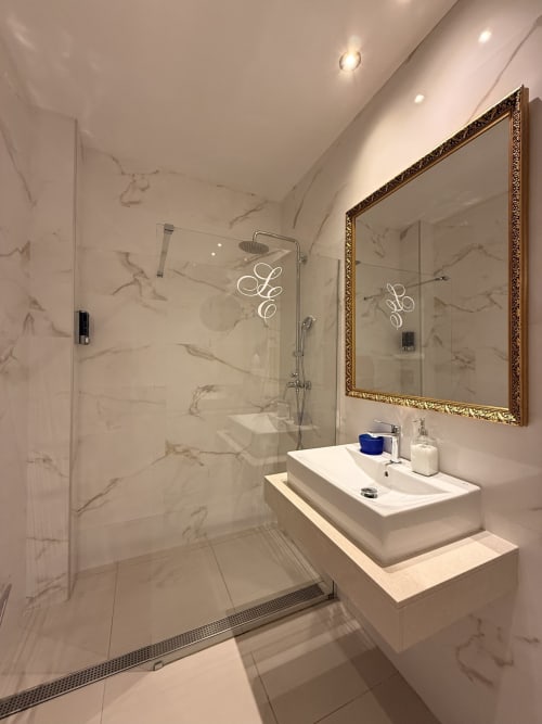 Baño de lujo en Edificio San Esteban 16 de Sevilla con revestimiento de mármol, cabina de ducha de cristal y espejo ornamental