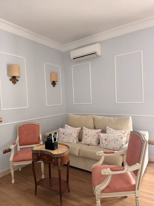 Elegante sala de estar de la suite Sevilla con sofá crema, cojines florales, sillas de terciopelo coral, paneles decorativos y aire acondicionado