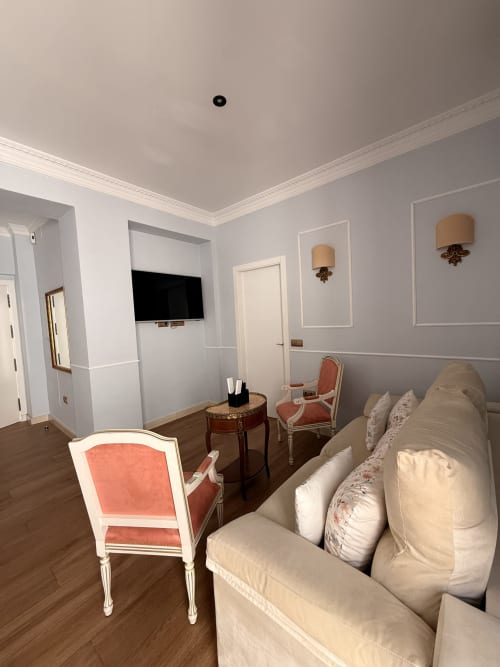 Elegante suite de dormitorio en Sevilla con sofá crema, sillón coral, televisor y muebles clásicos