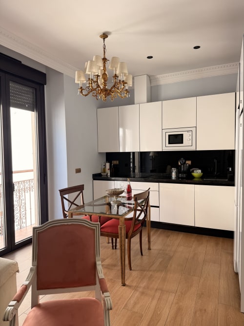 Cocina y comedor modernos de la suite Sevilla con muebles color crema, encimera negra, mesa de cristal y lámpara dorada