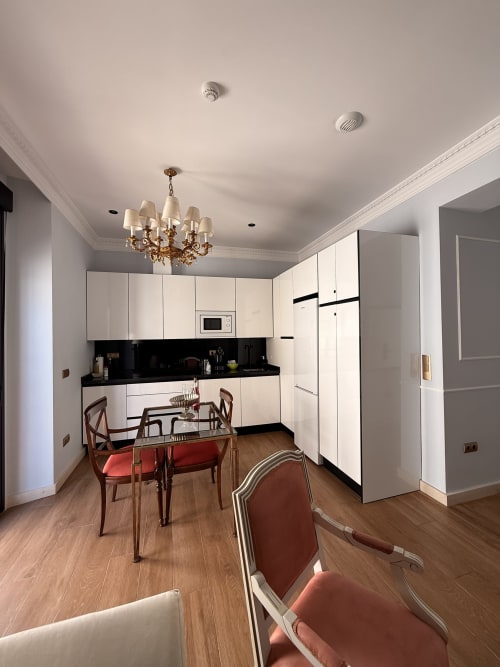 Cocina y comedor de suite de 1 dormitorio en hotel de Sevilla con muebles blancos, encimera negra y sillas de terciopelo rojo