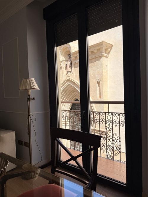 Balcón de hotel en Sevilla con vista a la Catedral Gótica a través de puertas francesas negras y barandilla de hierro forjado