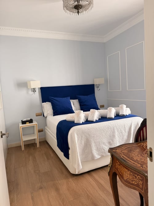 Suite moderna en Edificio San Esteban 16, Sevilla, con cabecero azul marino, ropa de cama blanca y piso de madera