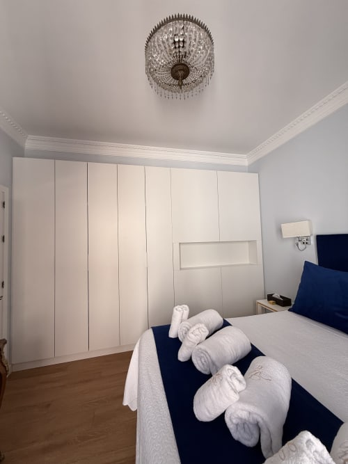 Suite dormitorio moderno en Edificio San Esteban 16, Sevilla con armario blanco, cama con toallas enrolladas, lámpara de techo de cristal
