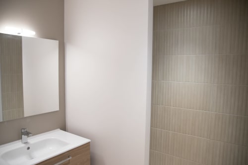Salle de bain moderne du Domaine de Castagnère avec lavabo blanc, miroir éclairant et douche en carrelage beige dans la chambre Aramis