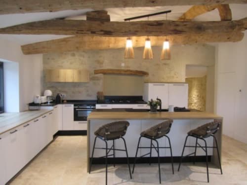 Cuisine moderne aux poutres en bois apparent, meubles blancs, îlot avec places assises et éclairage suspendu dans un cottage de la Drôme Provençale