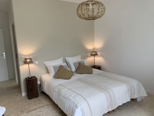Chambre moderne et lumineuse avec literie blanche, coussins olive, luminaire suspendu tissé et lampes de chevet à Domaine Maison Girardon