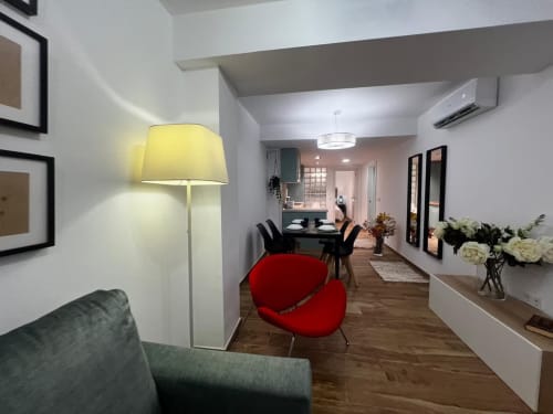 Moderno apartamento en Las Arenas Valencia con sillón rojo, lámpara de pie amarilla y cocina abierta al comedor